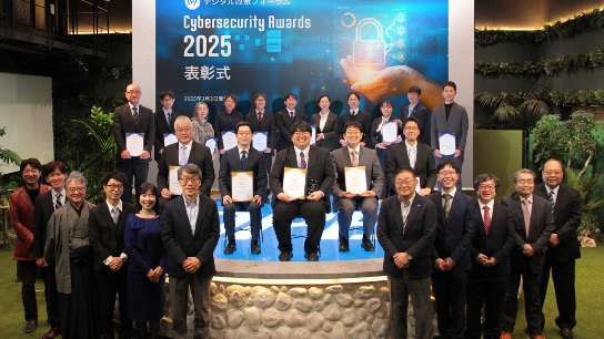 DPF デジタル政策フォーラム Cybersecurity Awards 2025 表彰式のステージで行われた集合写真。背景のスクリーンにはイベント名と日付が表示され、前列・中列・後列に参加者が並び、中列の人々は賞状のようなものを持っている。